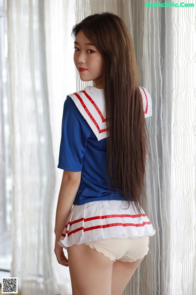 A woman in a sailor outfit standing by a window.