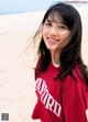 A woman in a red shirt standing on a beach.