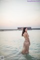 A woman in a long dress standing in the water.