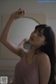 A woman in a pink tank top standing in front of a mirror.