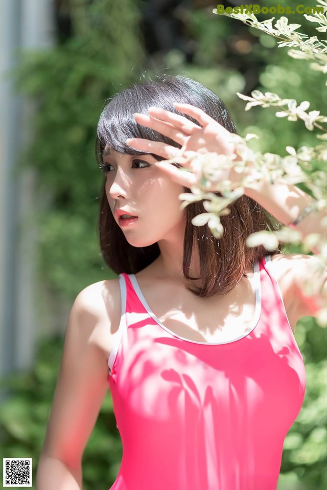 A woman in a pink tank top standing next to a bush.