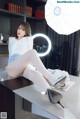 A woman sitting on top of a desk next to a lamp.