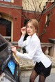 A woman in a white shirt and black skirt standing next to a car.