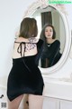 A woman in a black dress standing in front of a mirror.