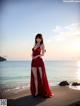 A woman in a red dress standing on a beach.