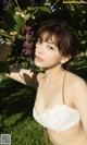 A woman in a white bra top holding a bunch of grapes.