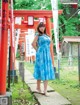 A woman in a blue dress standing in front of a red torii gate.