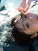 A little girl laying on a rock by the water.