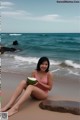 A woman in a pink bathing suit sitting on a beach holding a coconut.